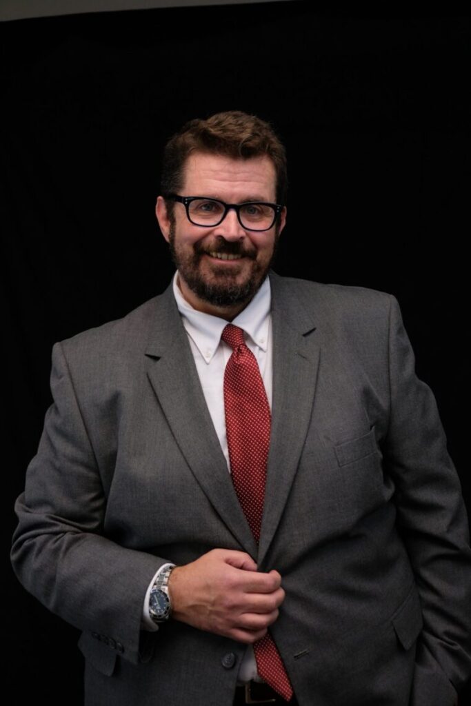 A portrait of attorney Charles Thomas, in a gray suit in front of a black background.